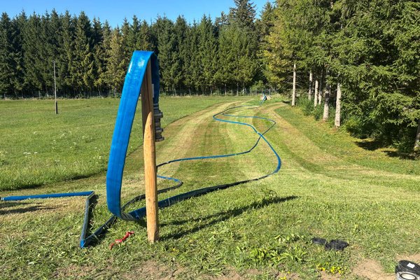 Blick auf Wiese, auf der Schläuche zum Brunnen zur Befüllung verlegt wurden
